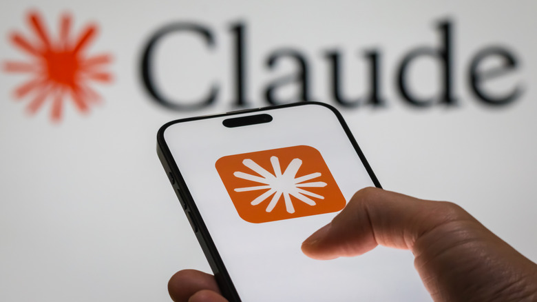 A hand holding a phone displaying the Claude logo.